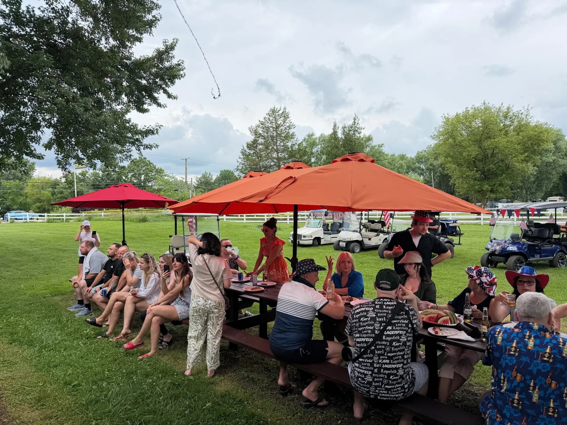Campers gathered at picnic tables under orange umbrellas